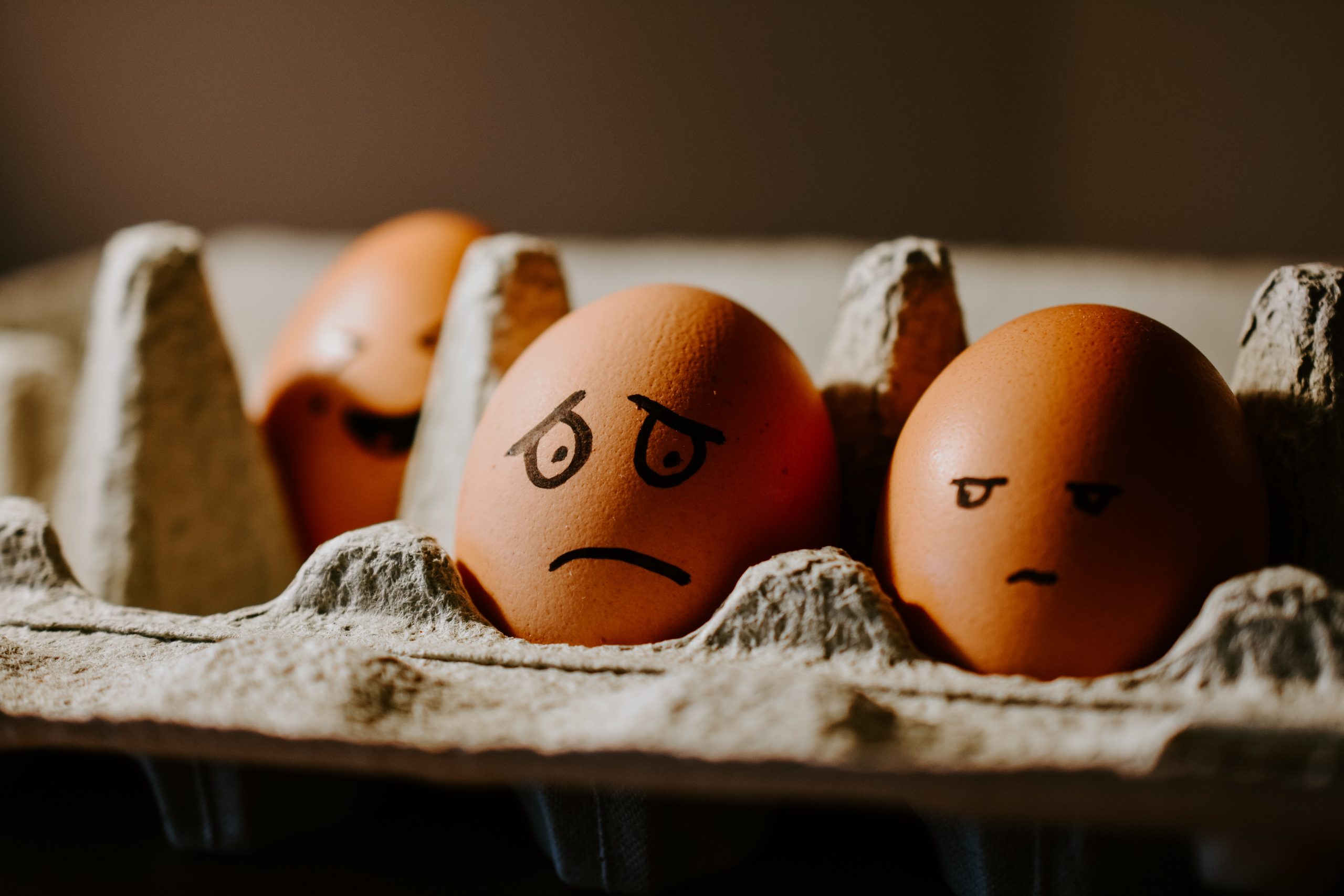 Eggs in a carton with faces drawn by a marker. One shows signs of worry.